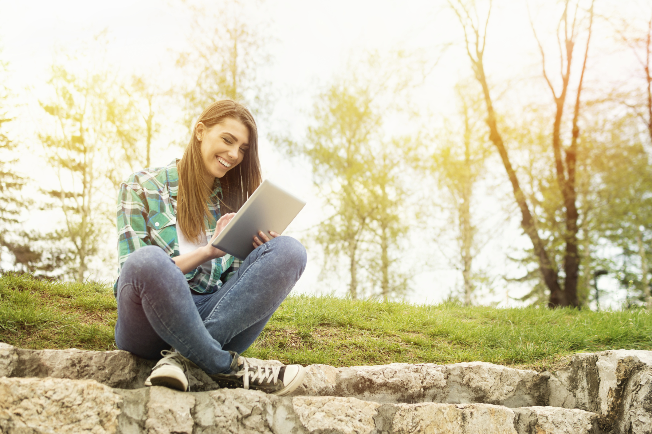 Happy young woman with digital tablet sitting in park